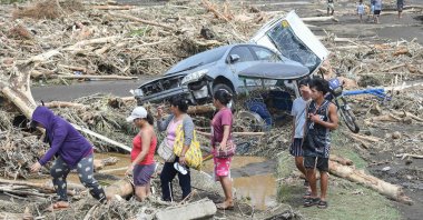 People walk past destroyed vehicles swept away along with debris of logs due to heavy rains brought about by Tropical Storm Trami in Laurel, Batangas province, Manila, Philippines, Oct. 25, 2024. (AFP Photo)