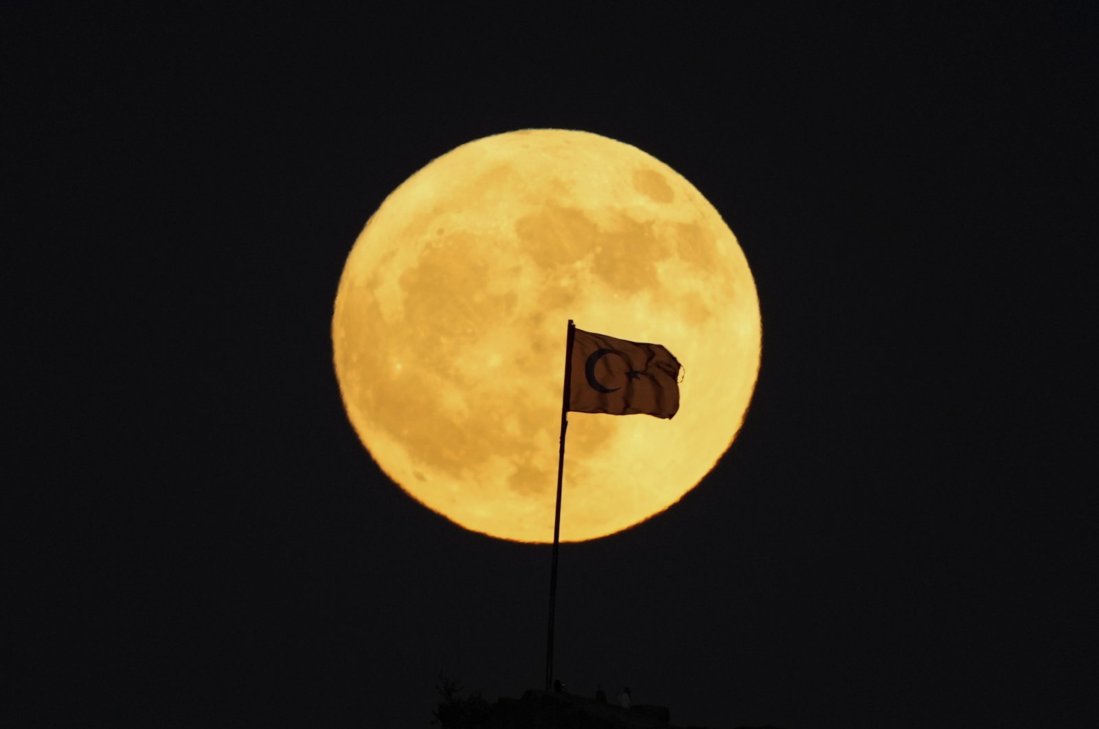 A Turkish flag is silhouetted against a full moon as it rises behind Afyonkarahisar Castle, Afyonkarahisar, central Türkiye, June 21, 2024. (AP Photo)