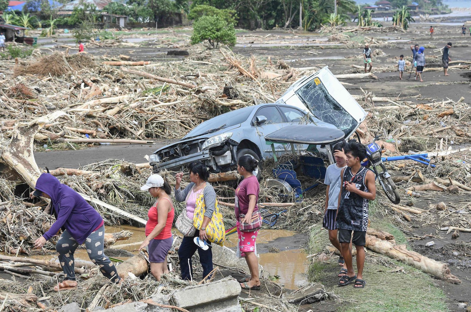 People walk past destroyed vehicles swept away along with debris of logs due to heavy rains brought about by Tropical Storm Trami in Laurel, Batangas province, Manila, Philippines, Oct. 25, 2024. (AFP Photo)