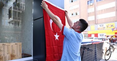 A shopkeeper hangs a Turkish flag on the facade of his shop in preparation for Republic Day celebrations in Denizli, western Türkiye, Oct. 23, 2024. (İHA Photo)