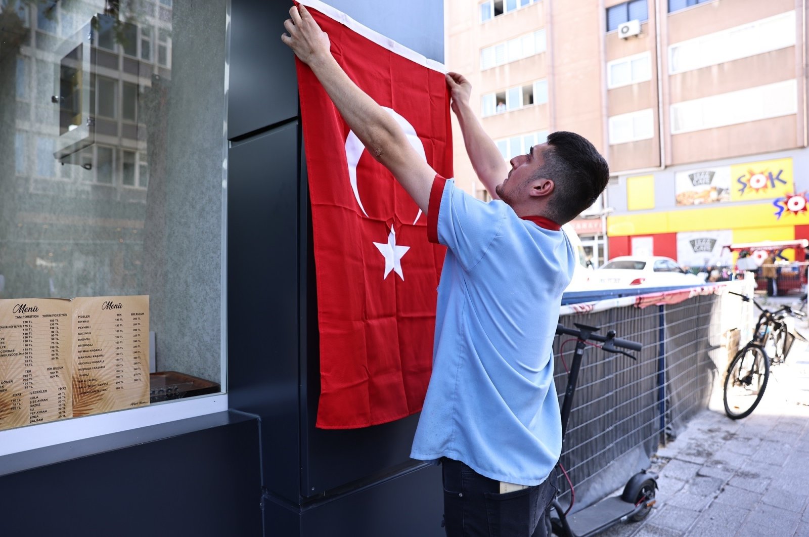 A shopkeeper hangs a Turkish flag on the facade of his shop in preparation for Republic Day celebrations in Denizli, western Türkiye, Oct. 23, 2024. (İHA Photo)