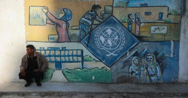A man squats by a wall bearing a mural representing the UNRWA at the aid agency's center at the Nuseirat camp for Palestinian refugees in the central Gaza Strip, Palestine, Oct. 29, 2024. (AFP Photo)
