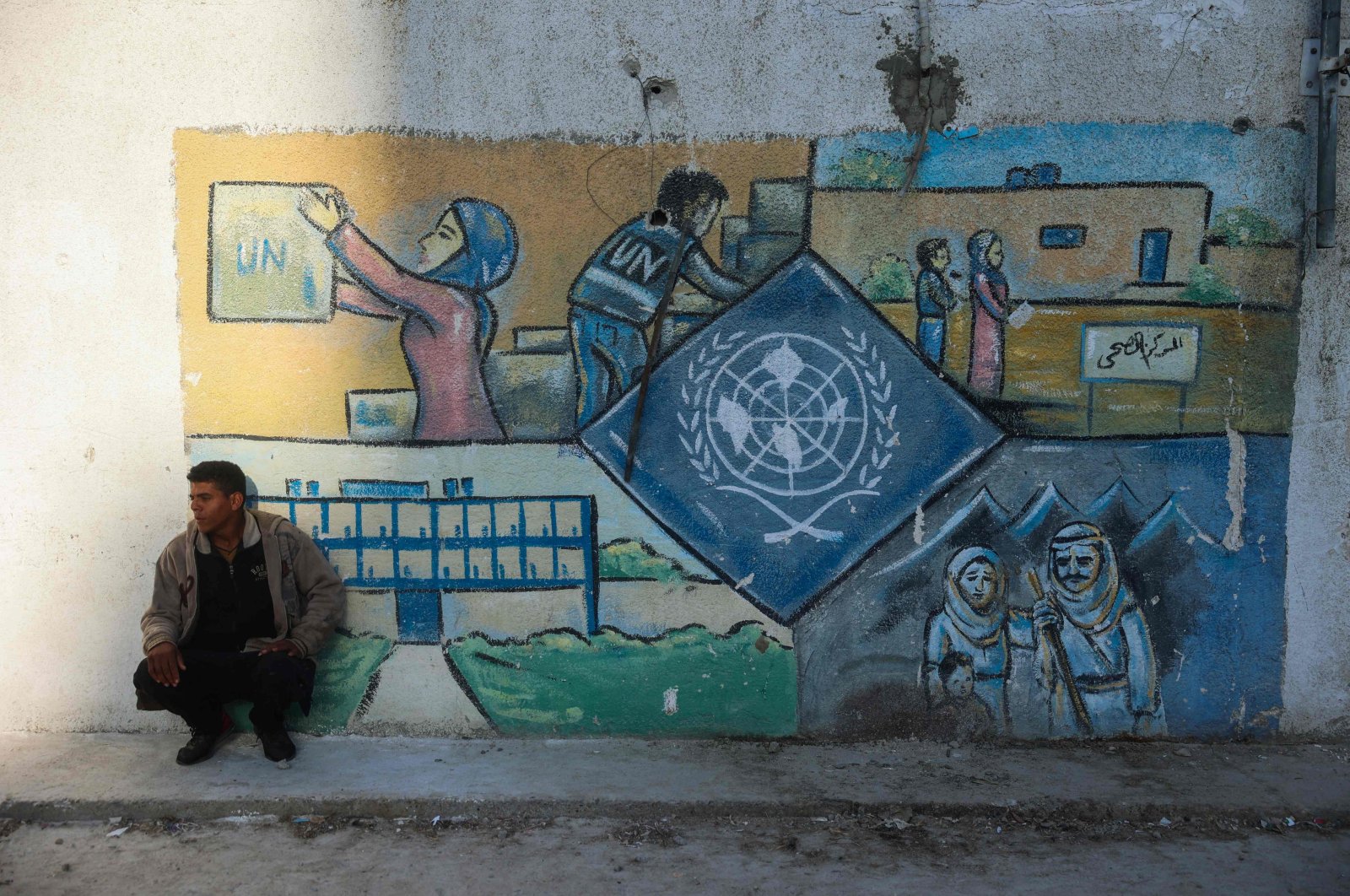 A man squats by a wall bearing a mural representing the UNRWA at the aid agency&#039;s center at the Nuseirat camp for Palestinian refugees in the central Gaza Strip, Palestine, Oct. 29, 2024. (AFP Photo)