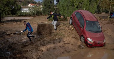 Men run next to a car covered with mud on a flooded street in Alora, near Malaga, Spain, Oct. 29, 2024. (AFP Photo)