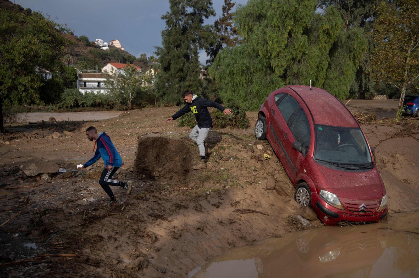 Men run next to a car covered with mud on a flooded street in Alora, near Malaga, Spain, Oct. 29, 2024. (AFP Photo)