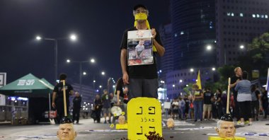 A demonstrator holding a portrait of an Israeli hostage held captive stands behind an installation of masks representing Israel's Prime Minister Benjamin Netanyahu during an anti-government protest calling for action to secure the hostages' release, in front of the Israeli Defense Ministry in Tel Aviv, Nov. 2, 2024. (AFP Photo)