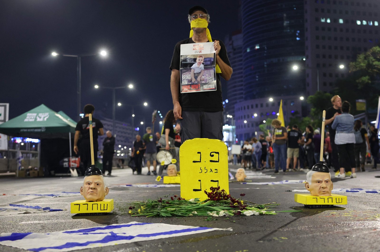 A demonstrator holding a portrait of an Israeli hostage held captive stands behind an installation of masks representing Israel&#039;s Prime Minister Benjamin Netanyahu during an anti-government protest calling for action to secure the hostages&#039; release, in front of the Israeli Defense Ministry in Tel Aviv, Nov. 2, 2024. (AFP Photo)