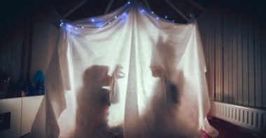 A parent and child tell each other stories inside a cosy tent lit up in a dark room of their home. (Getty Images)