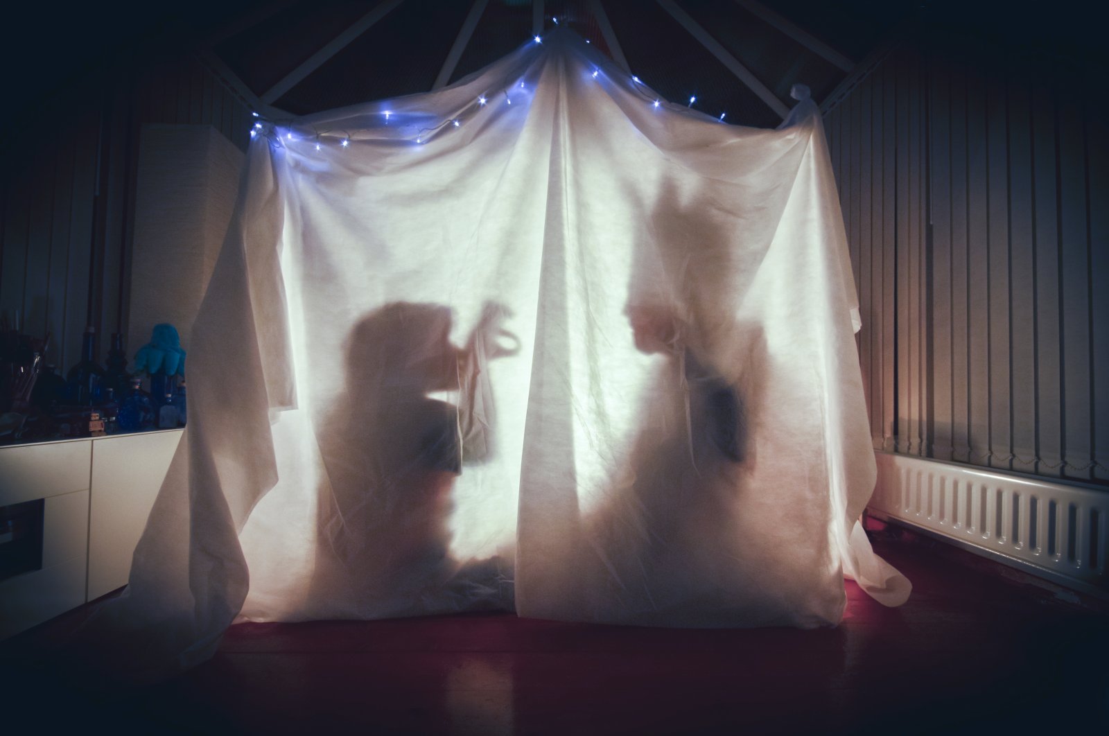 A parent and child tell each other stories inside a cosy tent lit up in a dark room of their home. (Getty Images)