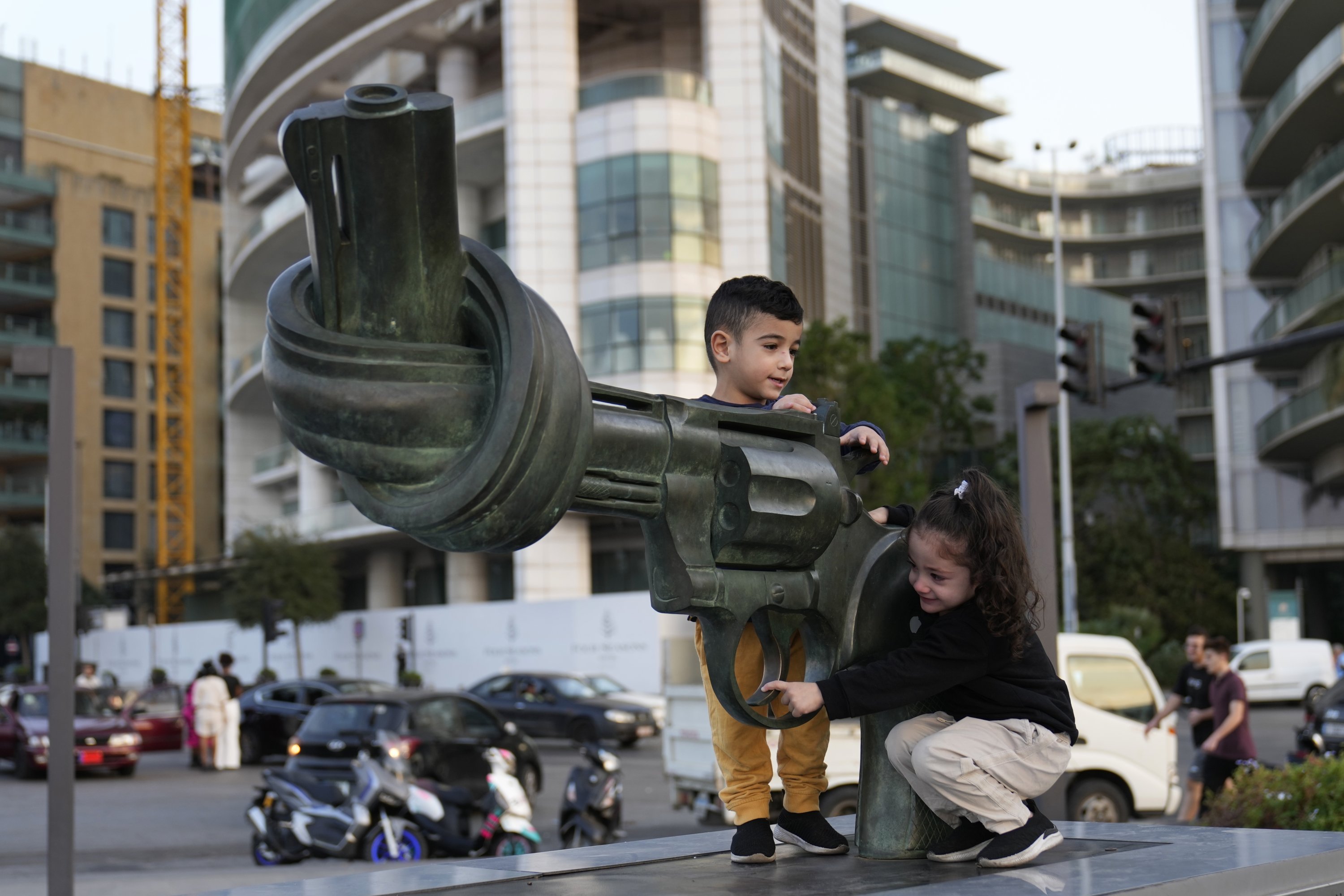 Hussein and Zahraa, 3, displaced Lebanese twins who fled with their parents from their village of Mais al-Jabal in south Lebanon, play on a gun with a twisted barrel statute, symbolizing anti-violence, in Beirut, Lebanon, Oct. 31, 2024. (AP Photo)