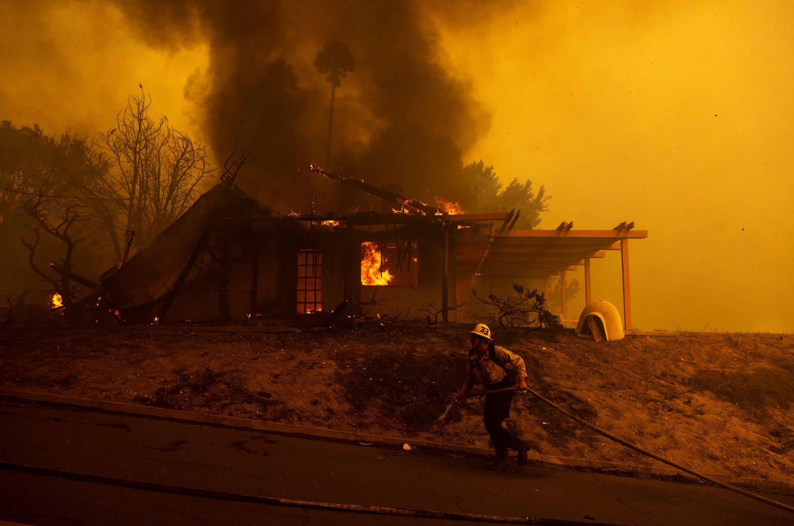 A firefighter pulls a hose in front of a burning house as the Mountain Fire scorches acres in Camarillo Heights, California, U.S., Nov. 6, 2024. (AFP Photo)