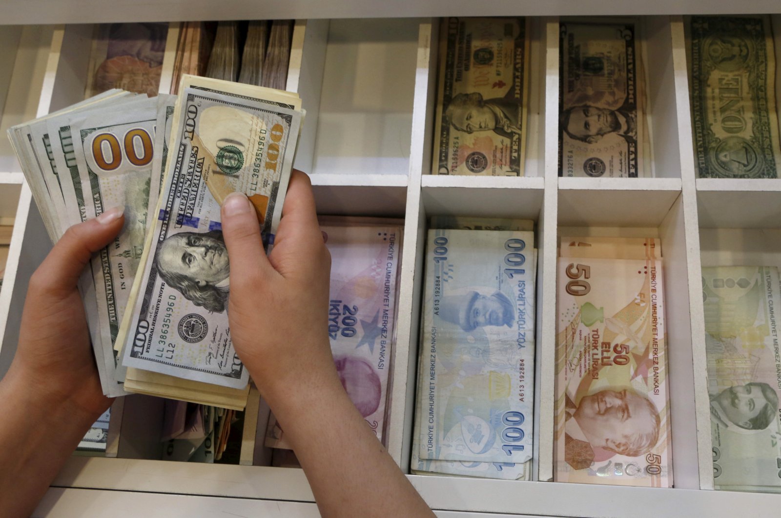 A money changer counts U.S. dollar bills, with Turkish lira banknotes in the background, at a currency exchange office in central Istanbul, Türkiye, Aug. 21, 2015. (Reuters Photo)