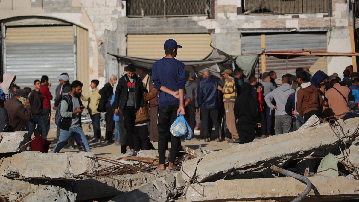 A Palestinian man holds a plastic bag with fresh bread and waits among the debris of buildings destroyed by Israeli airstrikes, Khan Younis, southern Gaza, Palestine, Nov. 20, 2024. (AFP Photo)