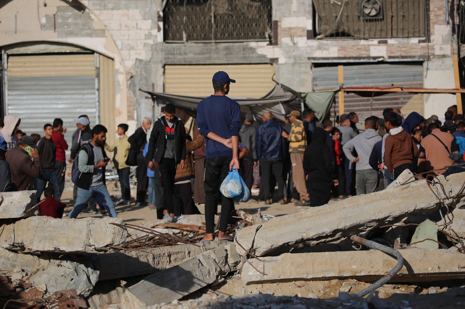 A Palestinian man holds a plastic bag with fresh bread and waits among the debris of buildings destroyed by Israeli airstrikes, Khan Younis, southern Gaza, Palestine, Nov. 20, 2024. (AFP Photo)