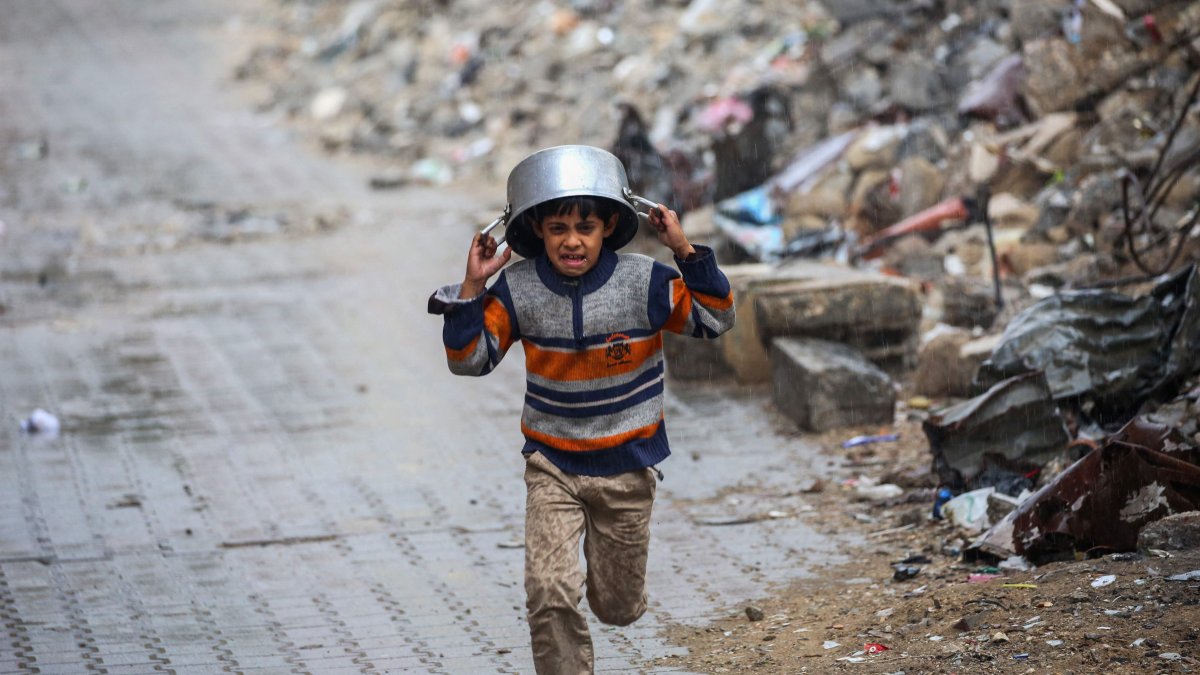 A displaced boy covers his head with a pan as he runs from the rain past buildings destroyed in Israeli attacks on the Bureij refugee camp, central Gaza Strip, Palestine, Nov. 24, 2024. (AFP Photo)