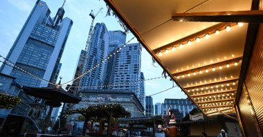 People walk through Christmas-themed booths in front of the banking district skyline, central Frankfurt, Germany, Nov. 21, 2024. (AFP Photo)