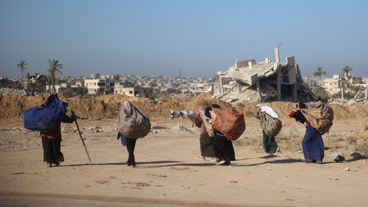 Women carry branches for a cooking fire on their backs as they walk past buildings destroyed in an Israeli bombing, Khan Younis, southern Gaza, Nov. 20, 2024. (AFP Photo)