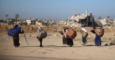Women carry branches for a cooking fire on their backs as they walk past buildings destroyed in an Israeli bombing, Khan Younis, southern Gaza, Nov. 20, 2024. (AFP Photo)