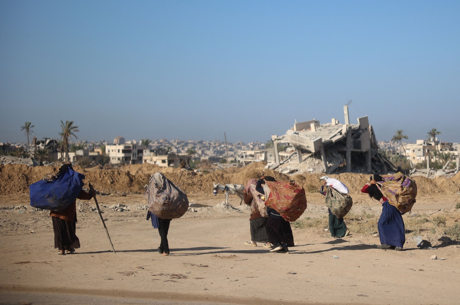 Women carry branches for a cooking fire on their backs as they walk past buildings destroyed in an Israeli bombing, Khan Younis, southern Gaza, Nov. 20, 2024. (AFP Photo)