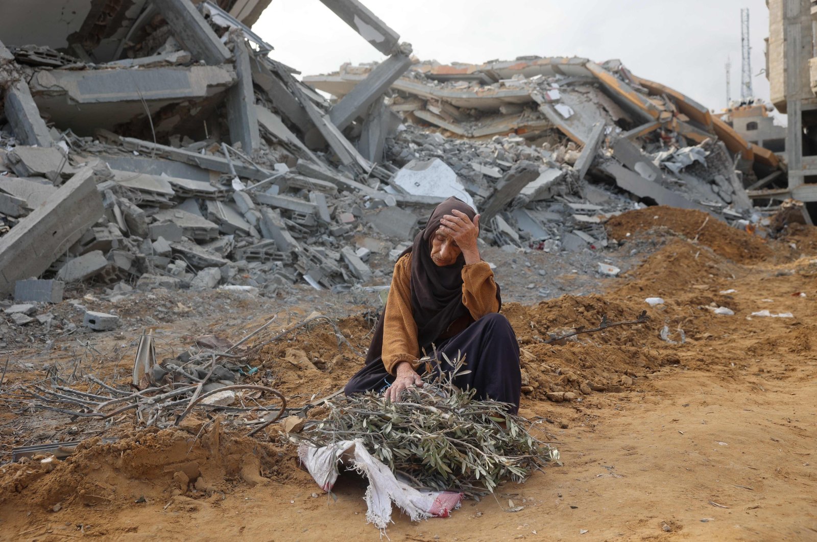 An elderly woman sits in front of a destroyed building to rest as she collects tree branches to light a fire in Nuseirat, Gaza Strip, Palestine, Nov. 29, 2024. (AFP Photo)