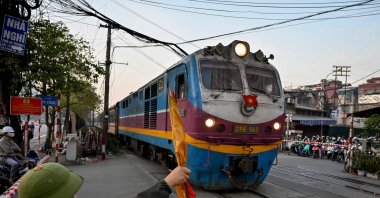 A railway worker holds a flag to signal safety for a passenger train passing through a railway crossing in Hanoi, Vietnam, Nov. 30, 2024. (AFP Photo)