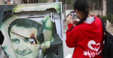 A woman takes a photo of a damaged picture of Syrian regime leader Bashar Assad, Qamishli, Syria, Dec. 8, 2024. (Reuters Photo)