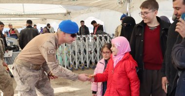 A Turkish soldier offers a candy bar to a Syrian girl returning home with her family through a border crossing in Hatay, southeastern Türkiye, Dec. 13, 2024. (AA Photo)
