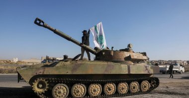 A Hayat Tahrir al-Sham (HTS) member stands atop a military vehicle as he carries a HTS flag in Saraqeb town in northwestern Idlib province, Syria, Dec. 1, 2024. (Reuters Photo)