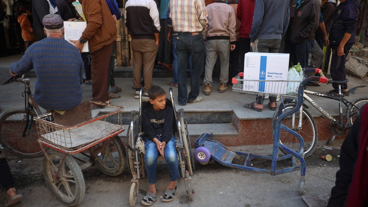 A boy rests in a wheelchair as people wait to receive humanitarian aid, supplied by the World Food Programme, in the Bureij refugee camp, central Gaza Strip, Palestine, Nov. 18, 2024. (AFP Photo)