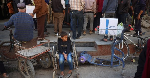 A boy rests in a wheelchair as people wait to receive humanitarian aid, supplied by the World Food Programme, in the Bureij refugee camp, central Gaza Strip, Palestine, Nov. 18, 2024. (AFP Photo)