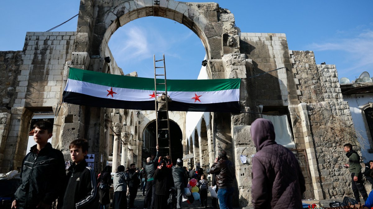 A person stands on a ladder next to the flag adopted by the new Syrian rulers on the day people attend Friday prayers after the ousting of Syria&#039;s Bashar Assad, Damascus, Syria, Dec. 20, 2024. (Reuters Photo)