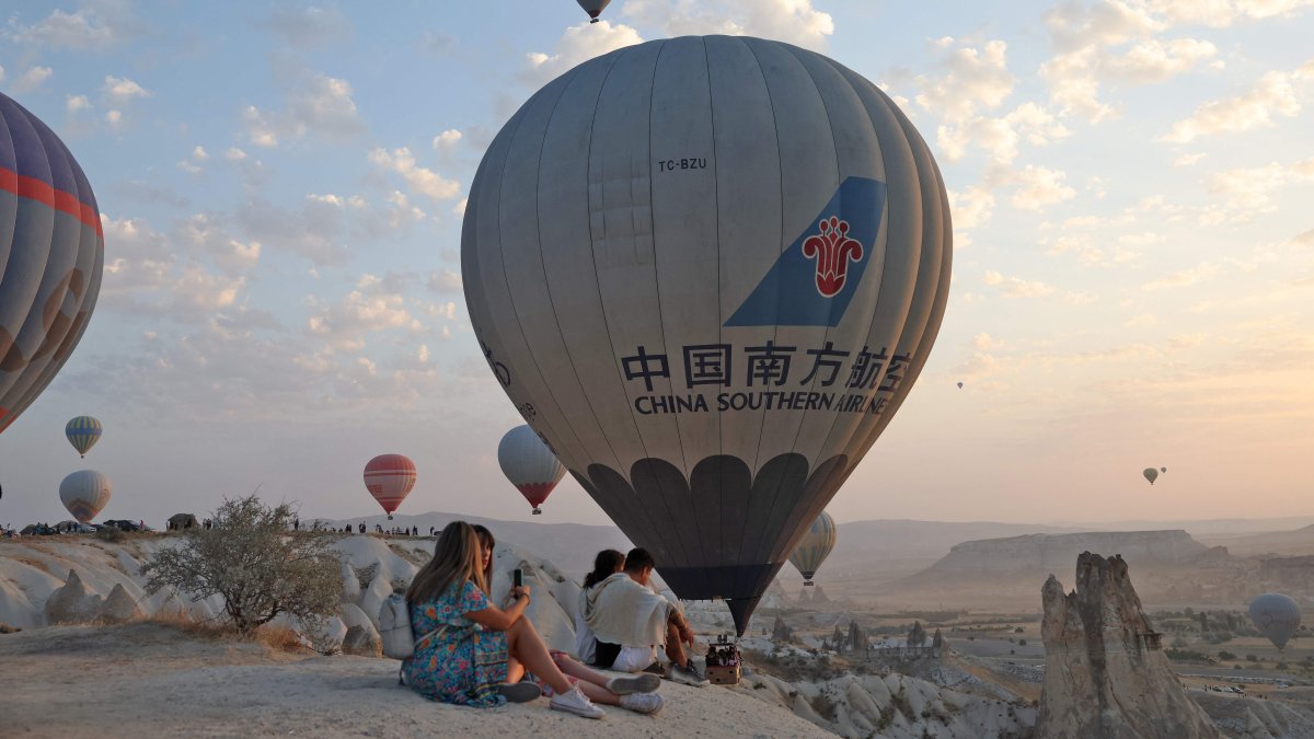 People sit along a promontory as sight-seeing hot air balloons launch in Göreme Historical National Park, east of Neveşehir in the province of the same name in central Türkiye&#039;s historical Cappadocia region, August 24, 2022. (AFP Photo)