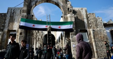 A person stands on a ladder next to the flag adopted by the new Syrian rulers on the day people attend Friday prayers after the ousting of Syria&#039;s Bashar Assad, Damascus, Syria, Dec. 20, 2024. (Reuters Photo)