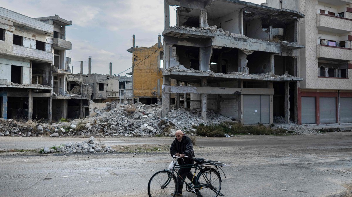 A Syrian man pushes his bicycle past damaged buildings, Homs, Syria, Dec. 20, 2024. (AFP Photo)