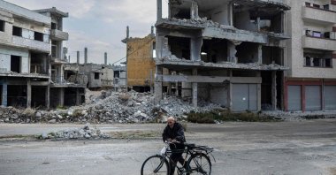 A Syrian man pushes his bicycle past damaged buildings, Homs, Syria, Dec. 20, 2024. (AFP Photo)
