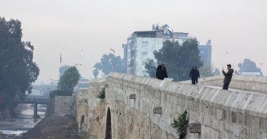 People walk across Taşköprü Bridge on a rainy winter day, Adana, Türkiye, Dec. 22, 2024. (IHA Photo)