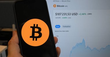 This illustration photograph shows the bitcoin cryptocurrency logo displayed on a smartphone beside a screen showing a trading chart, Brussels, Belgium, Dec. 17, 2024. (AFP Photo)