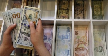 A money changer counts U.S. dollar bills, with Turkish lira banknotes in the background, at a currency exchange office in central Istanbul, Türkiye, Aug. 21, 2015. (Reuters Photo)