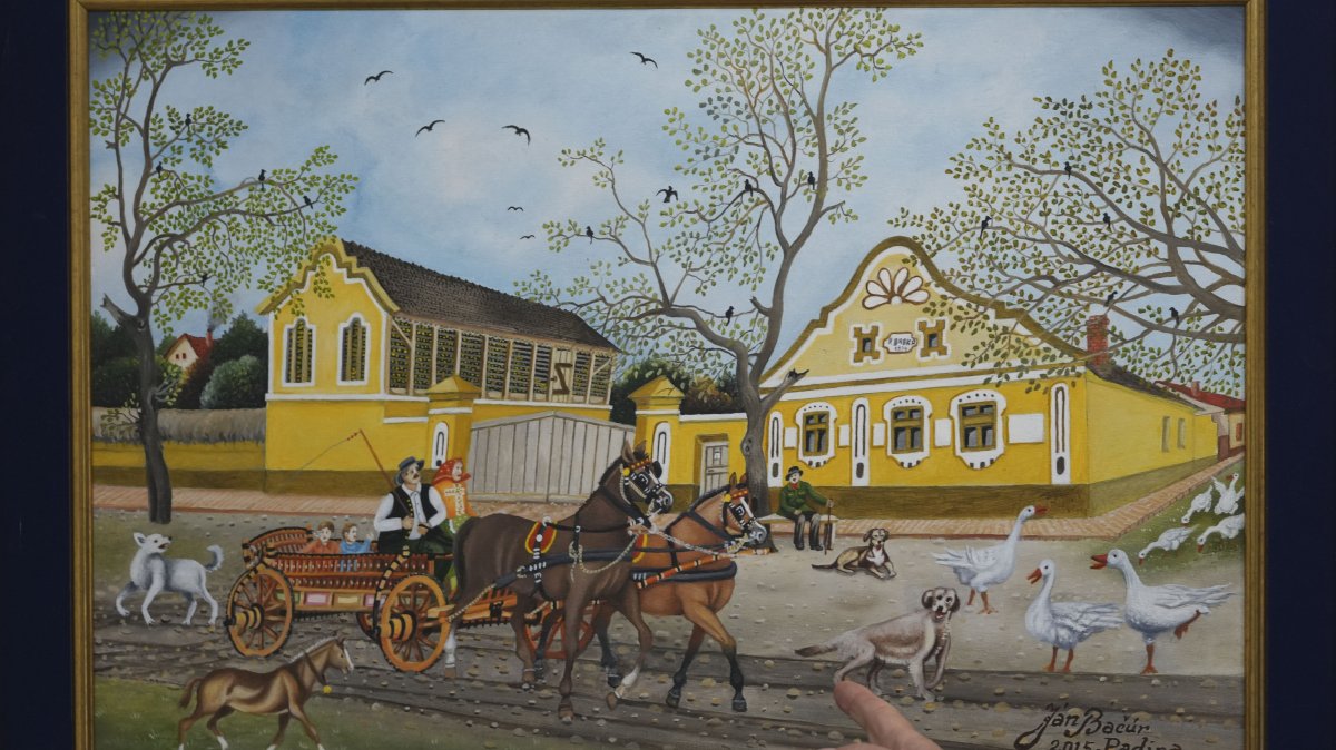 Pavel Babka, gallerist and naive art expert shows painting of a horse-drawn cart and a yellow house dating back to Austro-Hungarian times in the village of Kovacica, Serbia, Nov. 28, 2024. (AP Photo)