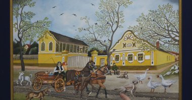 Pavel Babka, gallerist and naive art expert shows painting of a horse-drawn cart and a yellow house dating back to Austro-Hungarian times in the village of Kovacica, Serbia, Nov. 28, 2024. (AP Photo)