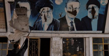 A worker tears down the pictures of Syria's former regime leaders Bashar Assad (L) and Hafez Assad (2nd R), Lebanon's late Hezbollah leader Sayyed Hassan Nasrallah (R) and Iran's Supreme Leader Ayatollah Ali Khamenei (2nd L) at a gas station in Nubl, Aleppo, Syria, Dec. 11, 2024. (Reuters Photo)