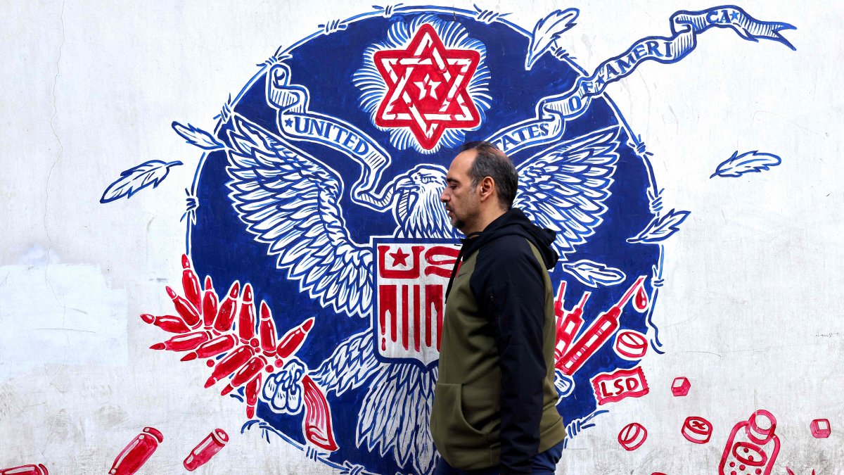 A man walks past graffiti depicting the Great Seal of the United States with a Star of David on top and a bald eagle clutching an ammunition belt and syringes in its claws, drawn on the walls of the former U.S. Embassy headquarters, Tehran, Iran, Dec. 30, 2024. (AFP Photo)