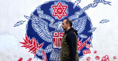 A man walks past graffiti depicting the Great Seal of the United States with a Star of David on top and a bald eagle clutching an ammunition belt and syringes in its claws, drawn on the walls of the former U.S. Embassy headquarters, Tehran, Iran, Dec. 30, 2024. (AFP Photo)