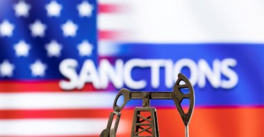A model of a pump jack is seen in front of the displayed word &quot;Sanctions&quot; and U.S. and Russia flag colors in this illustration created on March 8, 2022. (Reuters Photo)