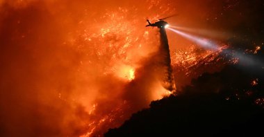 A fire fighting helicopter drops water as the Palisades fire grows near the Mandeville Canyon neighborhood and Encino, California, U.S., Jan. 11, 2025. (AFP Photo)