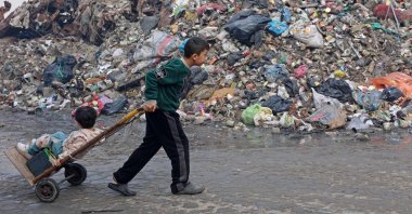 A Palestinian boy pulls a wheelbarrow with a child next to a garbage dumping site in Gaza City, Palestine, Jan. 11. (AFP Photo)