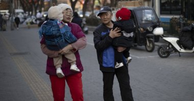 Two elders carry toddlers as they walk down a street, Beijing, China, Jan. 17, 2025. (EPA Photo)