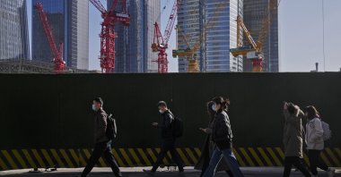 People wearing face masks walk by construction cranes near office buildings in the central business district, Beijing, China, March 15, 2023. (AP Photo)