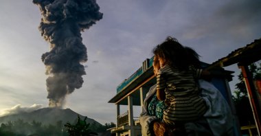 A woman and child look on at volcanic ash rising into the air during the eruption of Mount Ibu, as seen from Duono Village in West Halmahera, North Maluku province, Indonesia, Jan. 15, 2025. (AFP Photo)