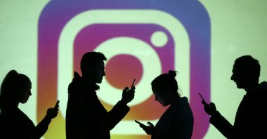 Silhouettes of mobile users are seen next to a screen projection of the Instagram logo in this picture illustration taken March 28, 2018. (Reuters Photo)